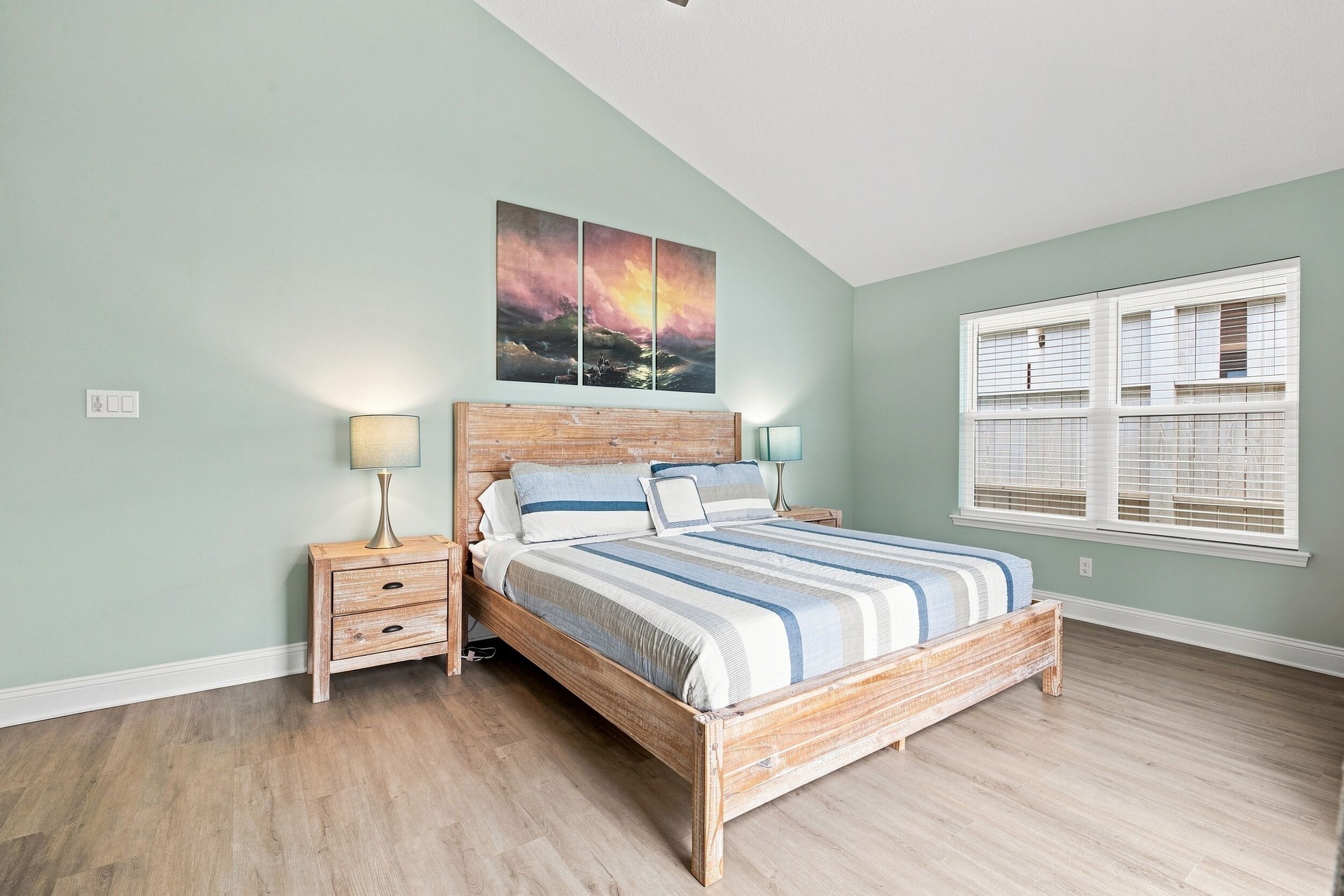 Une chambre à coucher avec un lit en bois, une table de chevet avec une lampe, une fenêtre avec des stores et un tableau au mur.