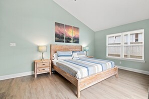 Ein Schlafzimmer mit einem hölzernen Bett, einem Nachttisch mit Lampe, einem Fenster mit Jalousien und einem Bild an der Wand.