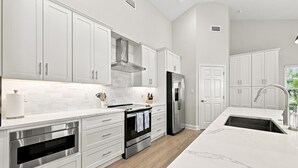 A modern kitchen with white cabinetry, stainless steel appliances, and a marble countertop. - Modern 3BR Near Beach | Good Morning Rentals (Jacksonville Beach)
