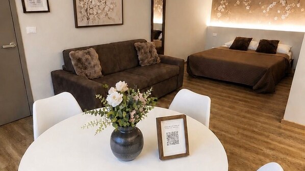 Ein Hotelzimmer mit einer Couch, einem Bett, einem Esstisch mit Blumenvase und einem gerahmten Bild.