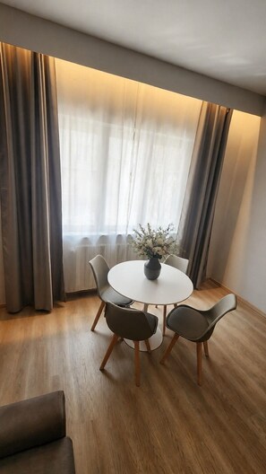 Een eetgedeelte met een ronde tafel, vier stoelen en een vaas bloemen.
