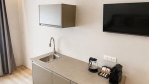 A modern kitchenette with a built-in sink, a coffee maker, and a flat-screen TV mounted on the wall. - ROOM 1 Studio apartment near downtown and the train station, with private parking (TORINO)