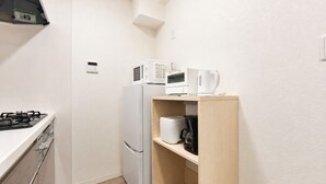 Uma cozinha compacta com fogão a gás, geladeira, micro-ondas, cafeteira e um armário com uma chaleira.