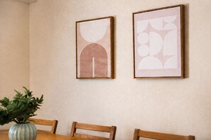 Ein Essbereich mit Tisch, Stühlen und zwei gerahmten Kunstwerken an der Wand.