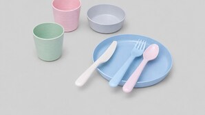 Conjunto de quatro peças de louça de cerâmica: uma chávena verde, uma chávena rosa, uma tigela cinzenta e um prato azul com um garfo e uma colher.