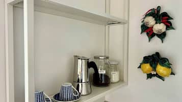 A kitchen shelf with a coffee maker, sugar jar, and a decorative wall hanging.