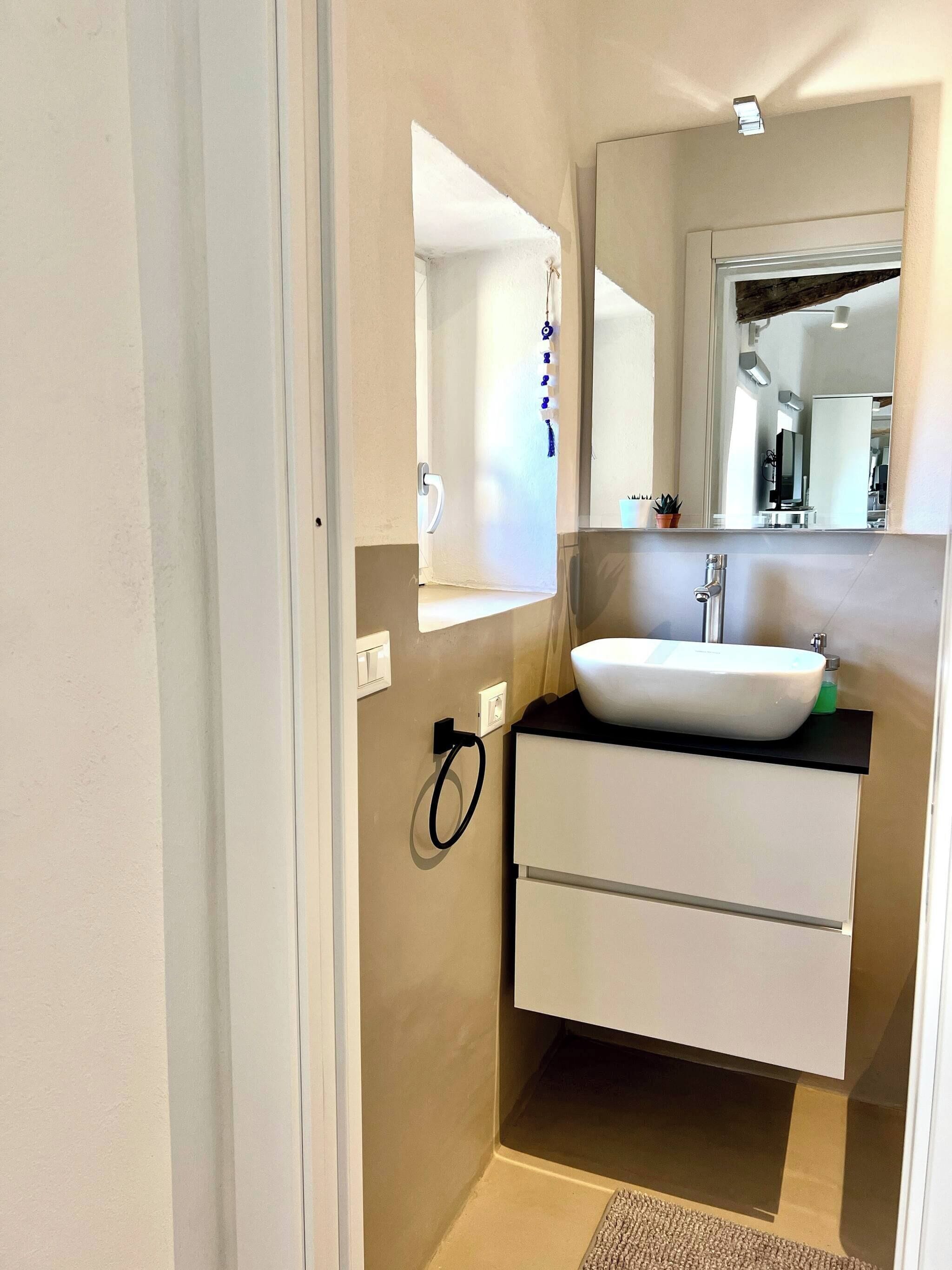 Un baño con lavamanos blanco, espejo y perchero.