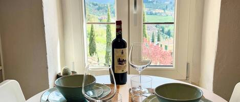 A dining table set with plates, glasses, and a bottle, with a view of a landscape through a window.