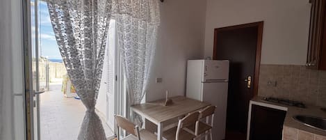 Ett kompakt kök med ett matbord och stolar, ett kylskåp och en liten arbetsbänk med en diskho.
