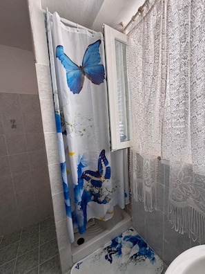 Ein Badezimmer mit Duschvorhang, der ein blaues Schmetterlingsmuster zeigt, einem Fenster mit weißem Rahmen und einem gemusterten Duschvorhang.