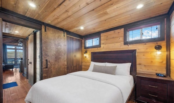 A wooden-paneled bedroom with a bed, a nightstand, and a window.