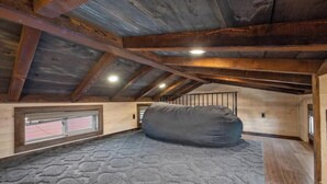 Ein Dachzimmer mit geneigter Decke, Holzbalken, einem großen Sitzsack und einem Fenster.