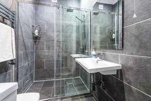 Ein modernes Badezimmer mit einer gläsernen Dusche, einem weißen Waschbecken und einem großen Spiegel.