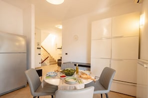 A modern kitchen with a dining table set for two, a refrigerator, and a staircase leading to an upper level. - ALL MareVista | 5-Bedroom Coastal Retreat with Sea-View Terrace (Bari)
