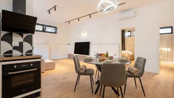 A modern kitchen with a built-in oven, a dining area with a round table and chairs, and a flat-screen TV mounted on the wall.