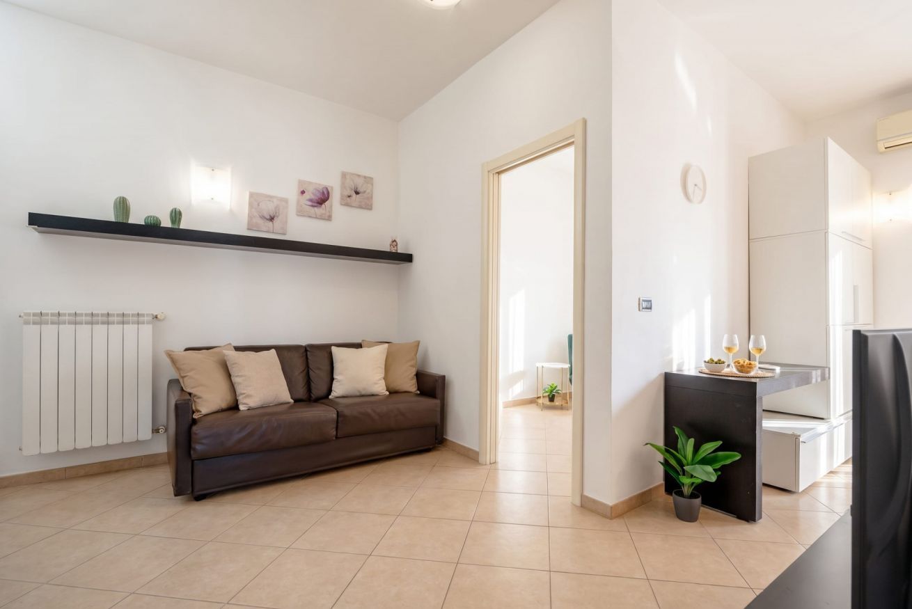 Ein modernes Wohnzimmer mit einer Couch, einem Heizkörper, einem Regal mit Dekoration und einer Tür zu einem anderen Raum.