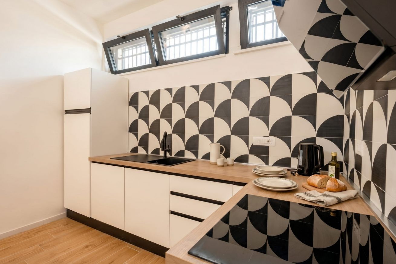 Una cucina moderna con zoccolo a mosaico geometrico, un piano di lavoro in legno e forno integrato.