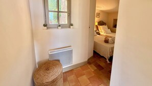 Un couloir étroit avec un radiateur, une fenêtre donnant sur un espace verdoyant et un lit avec une tête de lit et des oreillers.