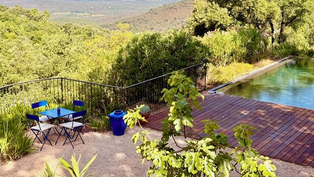 Une terrasse avec une piscine, entourée de verdure et offrant une vue sur un paysage.
