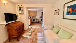 Un salon avec un canapé, une table basse, un téléviseur et, au fond, une cuisine.