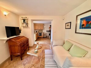 A living room with a sofa, a coffee table, a TV, and a kitchen in the background. - Le Bastidon (La Garde-Freinet)