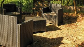 Outdoor wicker furniture arranged in a semi-circle, surrounded by a natural setting with trees and a wooden fence. - Handbuilt home in the wild Ligurian hills (Pontinvrea)