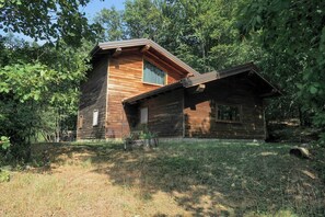 Eine Holzhütte mit geneigtem Dach, umgeben von Bäumen und Gras.