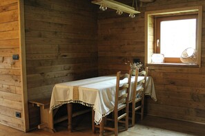 A wooden cabin room with a small table and chairs, a window with a basket, and a light fixture. - Handbuilt home in the wild Ligurian hills (Pontinvrea)