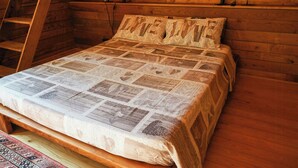 A wooden bed with a quilted bedspread in a cabin-style room with a ladder and wall-mounted lamps.