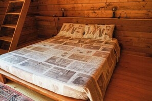 A wooden bed with a quilted bedspread in a cabin-style room with a ladder and wall-mounted lamps.