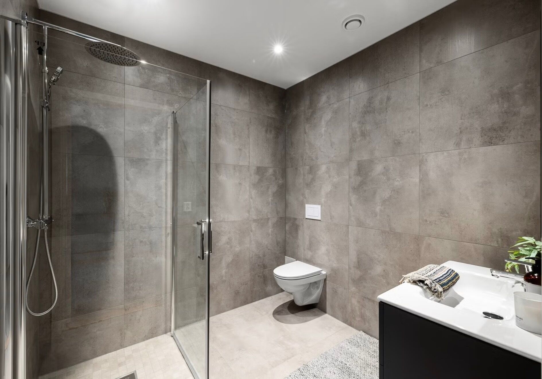 A modern bathroom with a glass-enclosed shower, a toilet, and a sink with a towel.