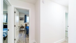 Un couloir menant à une chambre à coucher, où se trouvent un lit, une table de chevet et un tableau accroché au mur.