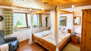 Una cama con dosel sobre un suelo de madera, una ventana con cortinas, una mesita de noche con una lámpara y un espejo en la pared.