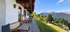 Eine Holzterrasse mit Sitzgelegenheiten im Freien, ein Steinweg und ein Blick auf die Berge.
