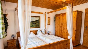 Uma cama de madeira com dossel, uma mesa de cabeceira com abajur e um quadro na parede.