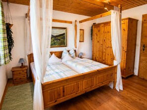 Ein hölzernes Himmelbett mit Baldachin, ein Nachttisch mit Lampe und ein Gemälde an der Wand.