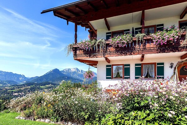 Una chaleta tradicional con un balcón decorado con flores, vistas a la montaña y un jardín exuberante.