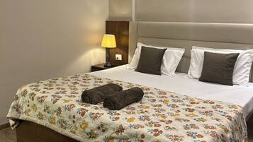 A hotel room with a bed, a nightstand with a lamp, a remote control, and wall art.