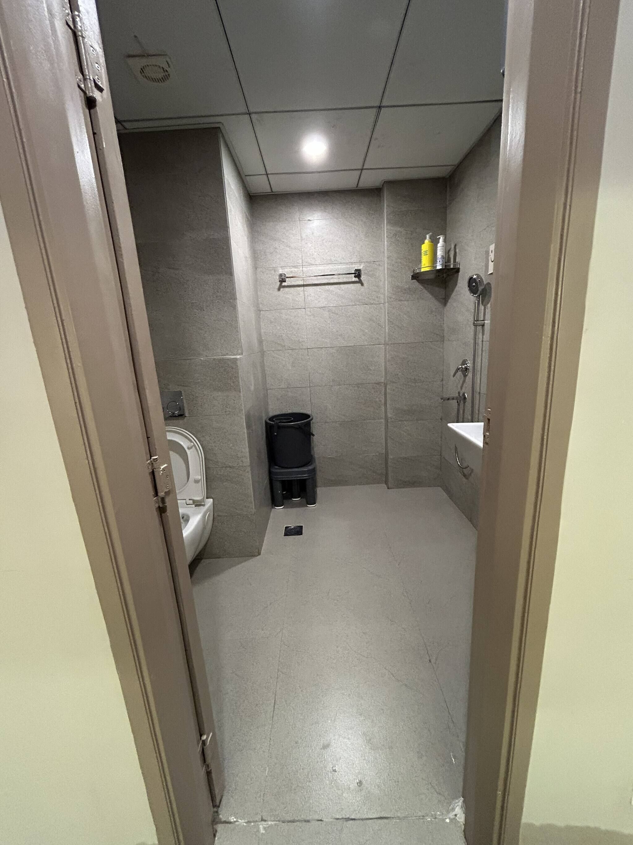 Un baño pequeño y cerrado con inodoro, un cubo de basura y zona de ducha.