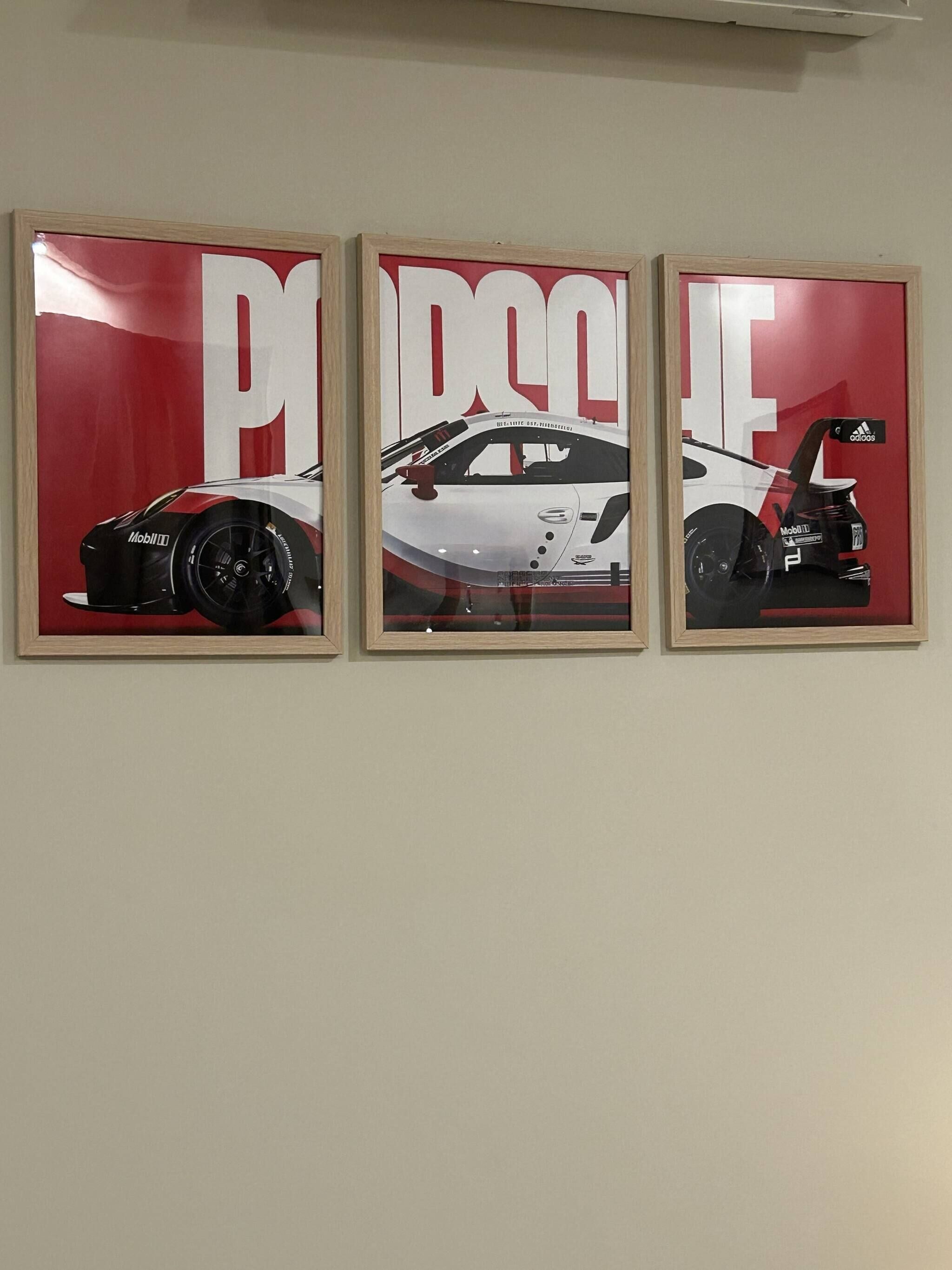 Three framed posters of a white car with red accents on a wall.