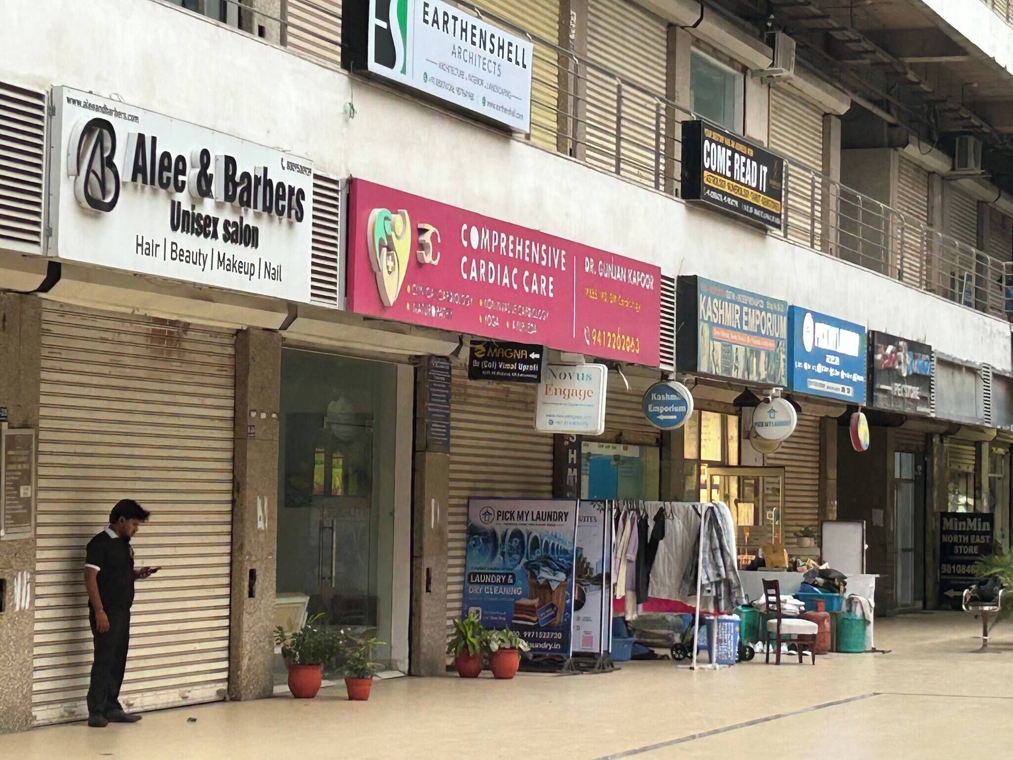 A row of commercial buildings with various storefronts, including a barber shop, a cardiac care clinic, and a clothing store.