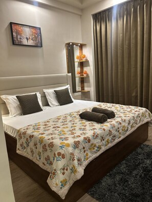 Cama bem arrumada com colcha florida, dois travesseiros e duas toalhas enroladas.