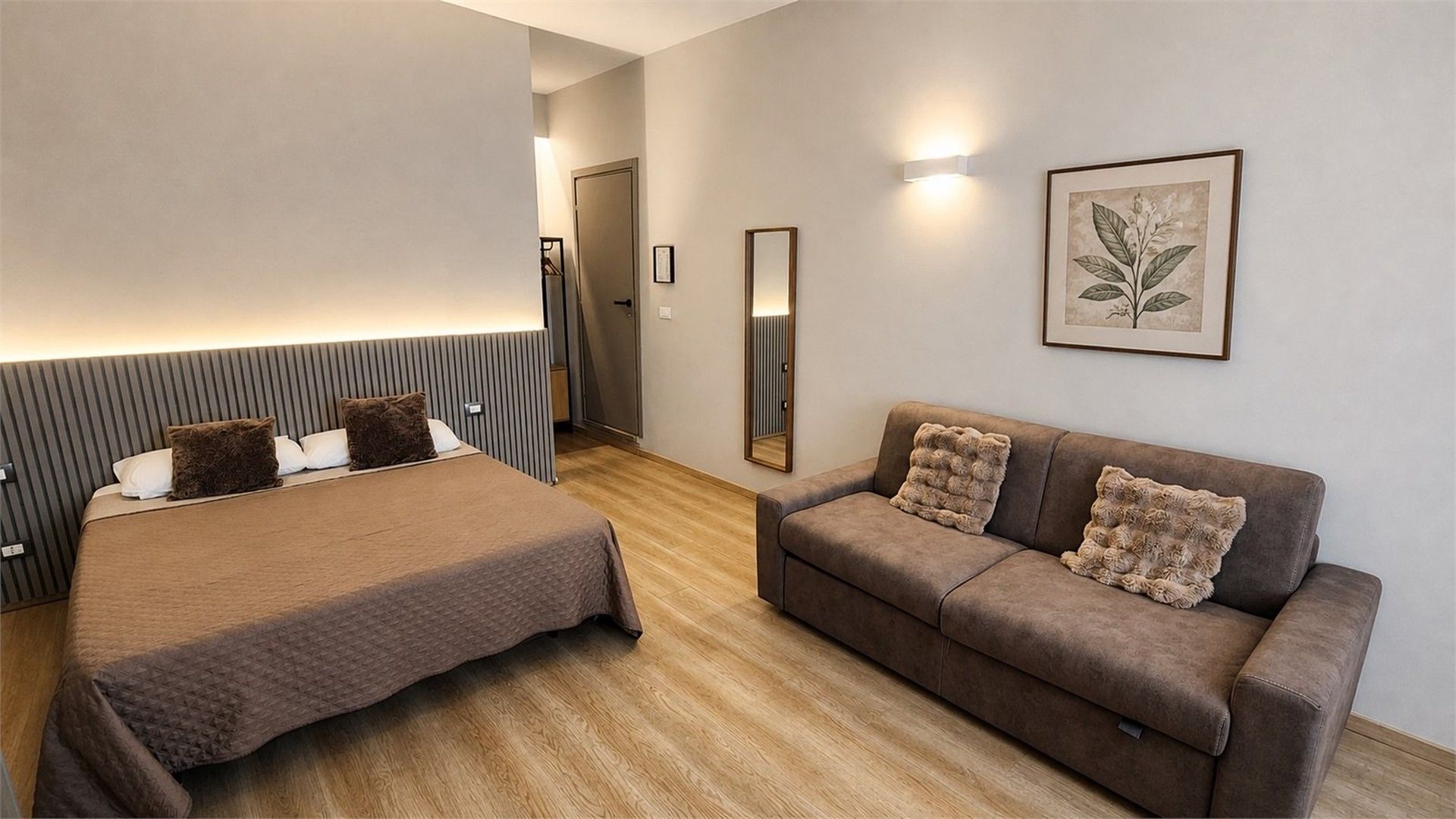 Une chambre d’hôtel avec un lit, un canapé, un miroir et une estampe botanique encadrée au mur.