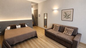 Et hotelværelse med en seng, en sofa, et spejl og et indrammet blomsterprint på væggen.