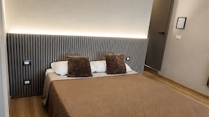 Et hotelværelse med en seng, en sengegavl med lodrette linjer, to puder og en dør.