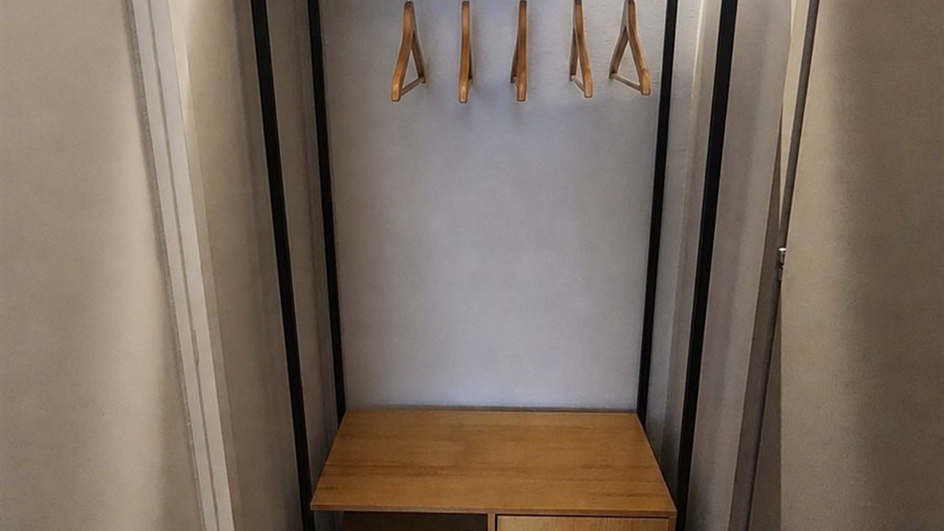 Un petit banc en bois, placé dans un coin, avec un porte-manteau fixé au mur juste au-dessus.