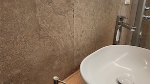 A bathroom with a white sink, a shower area, and a textured wall. - Room 3 (Torino)