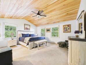Ein Schlafzimmer mit Bett, Sitzbank, Nachttisch, Kommode und Deckenventilator.