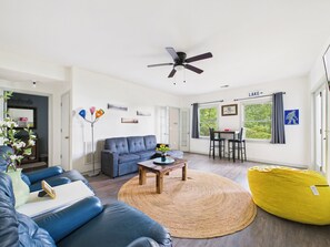 A modern living room with a sofa, coffee table, and a yellow bean bag. There is a dining area with a table and chairs. - NEW LISTING! Koi Pond Lodge by Chatuge Home Concierge | Near Lake Chatuge & Mountain Views (HIAWASSEE)
