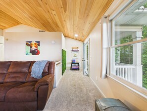 Ein gemütliches Interieur mit einem braunen Ledersofa, einem Kühen-Bild und Blick durch ein großes Fenster.